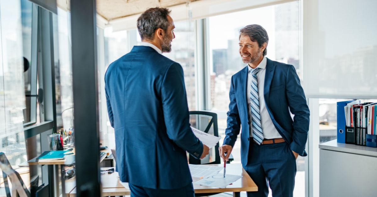 Dos empresarios discutiendo en oficina con vista a la ciudad
