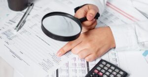 Persona revisando documentos con lupa y calculadora