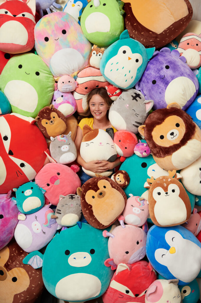 Niña sonriendo rodeada de peluches coloridos