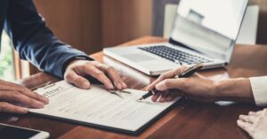 Personas firmando contrato con laptop en mesa de madera