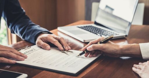 Personas firmando contrato con laptop en mesa de madera