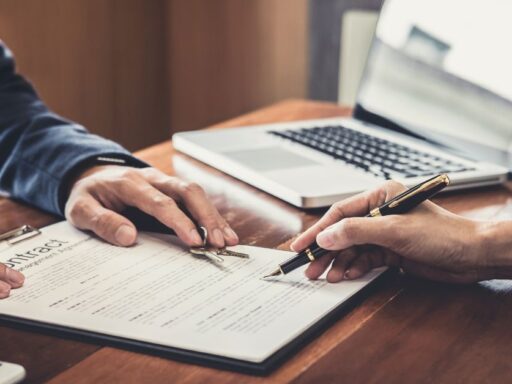 Personas firmando contrato con laptop en mesa de madera
