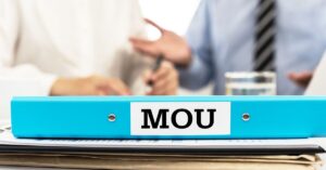 Carpeta 'MOU' sobre escritorio con gente de fondo
