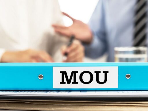 Carpeta 'MOU' sobre escritorio con gente de fondo