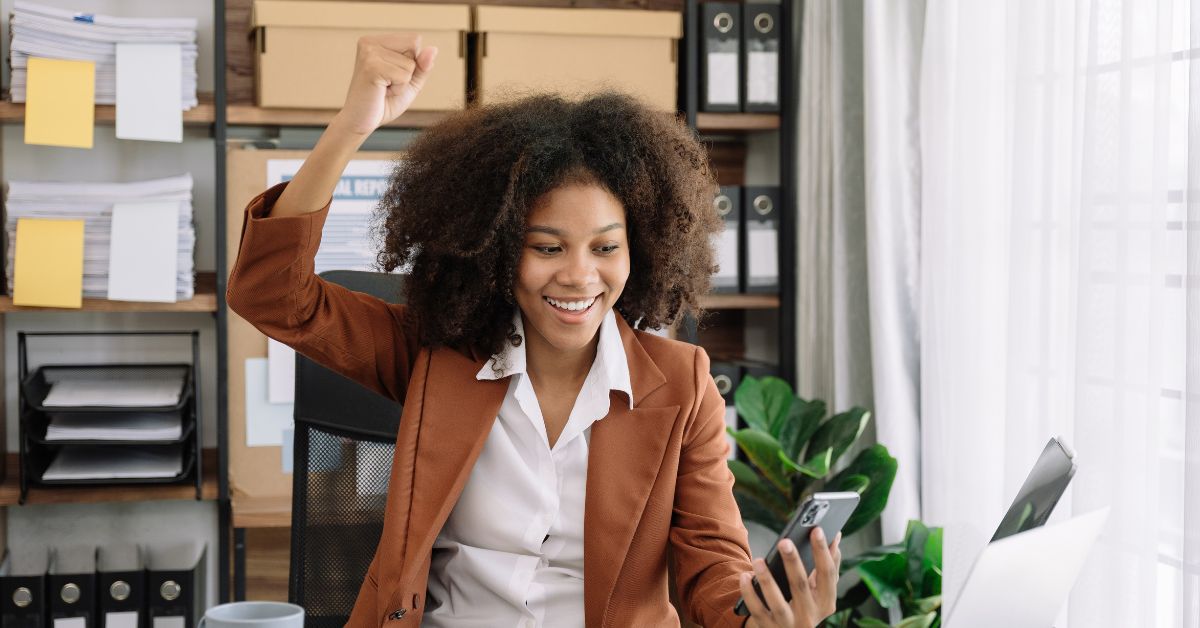 Mujer celebrando éxito con celular en oficina
