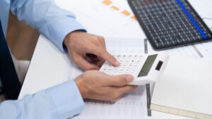 Persona calculando finanzas con calculadora y laptop