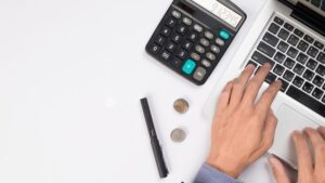 Mano trabajando con calculadora y laptop en escritorio
