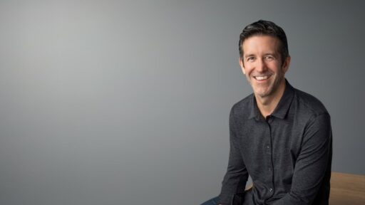 Hombre sonriente sentado frente a fondo gris