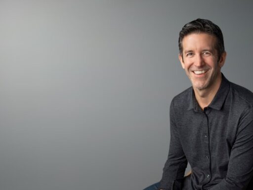 Hombre sonriente sentado frente a fondo gris